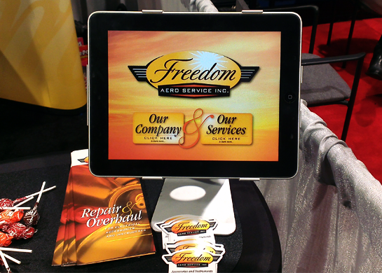 iPad Kiosk for trade show. Tap on one of the large buttons and the screen scrolls left or right to a 3 minute video – one on the Company and one on Services provided. Shown with trade-show handouts – brochures, refrigerator magnets and Tootsie Pops.